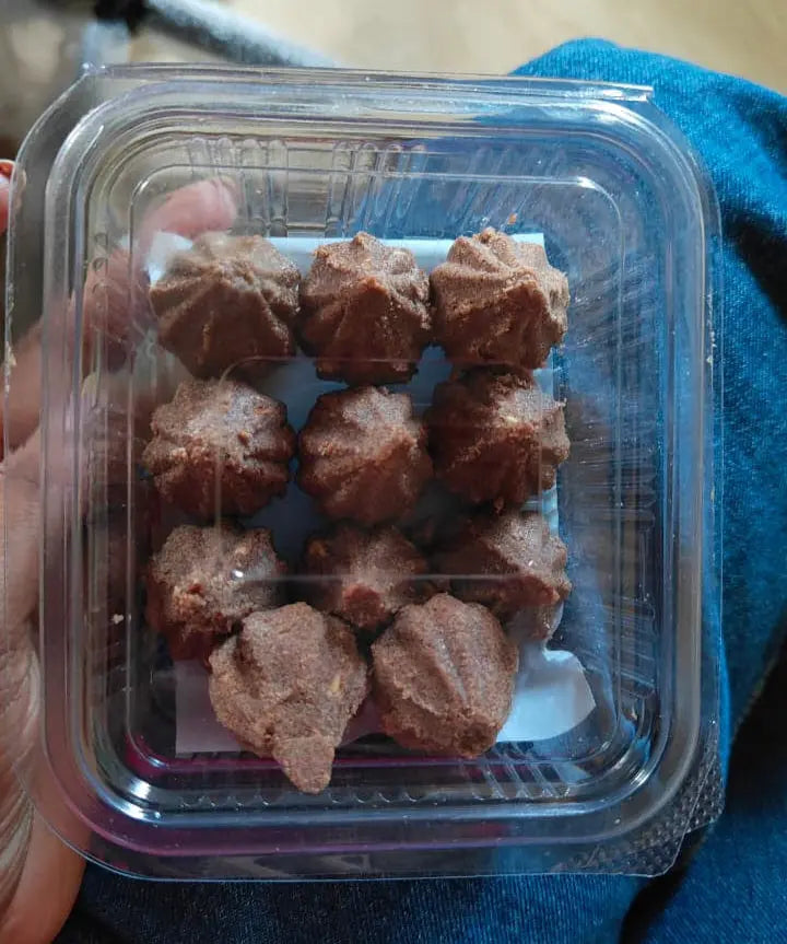 Container of millet laddo held by a person on a blue surface